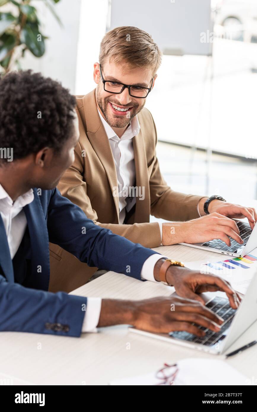 two multiethnic businessmen using laptops at table in office Stock Photo