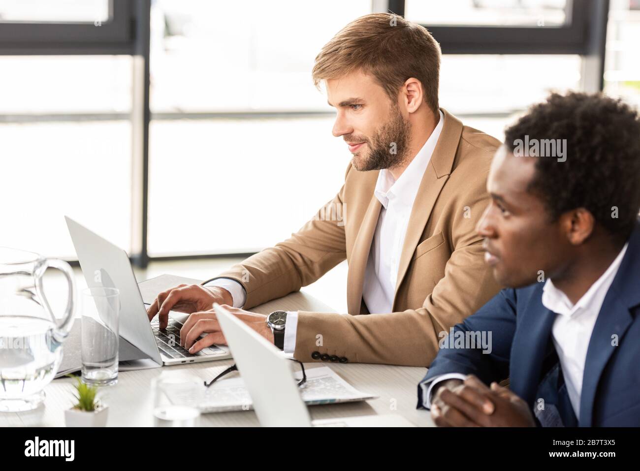 two multiethnic businessmen using laptops at table in office Stock Photo