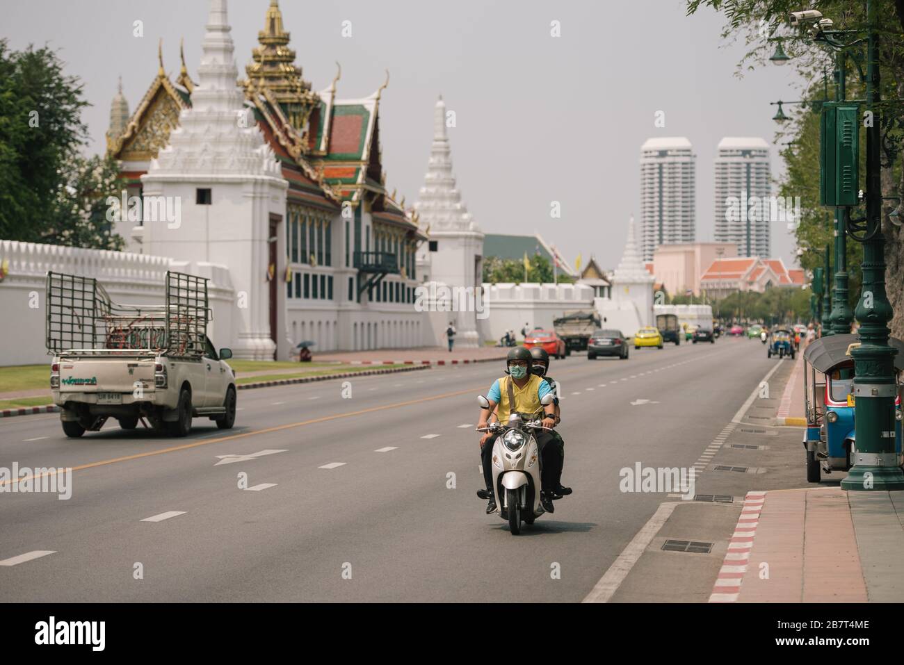 A motorbike passes the Grand Palace with the driver and passenger both wearing protective face masks Stock Photo
