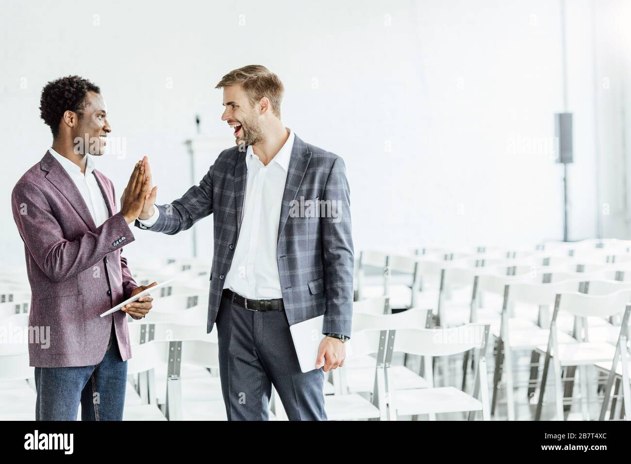 two multiethnic colleagues in formal wear holding digital tablets in conference hall Stock Photo