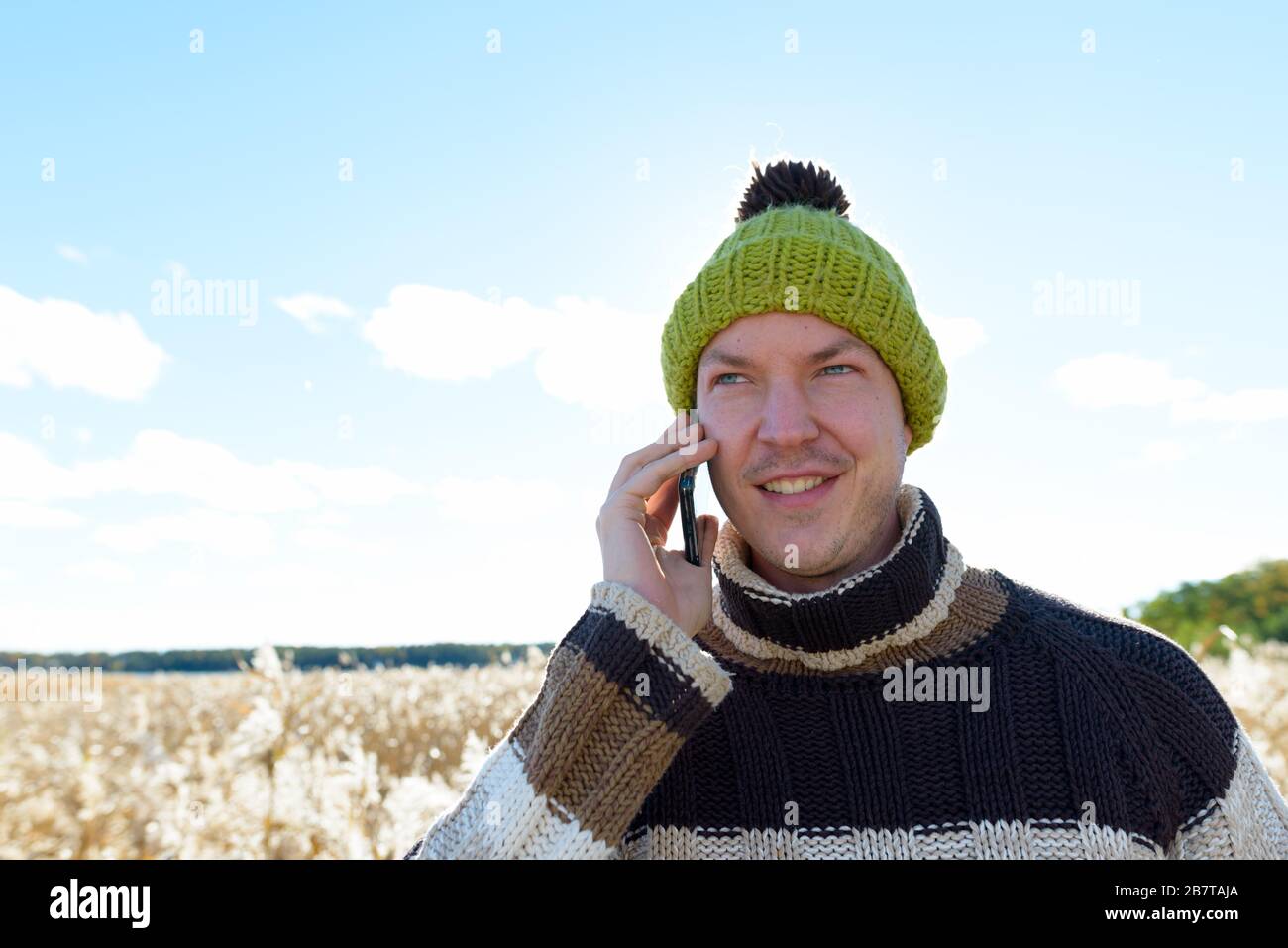 Happy young handsome man talking on the phone against scenic view of autumn bulrush field Stock Photo