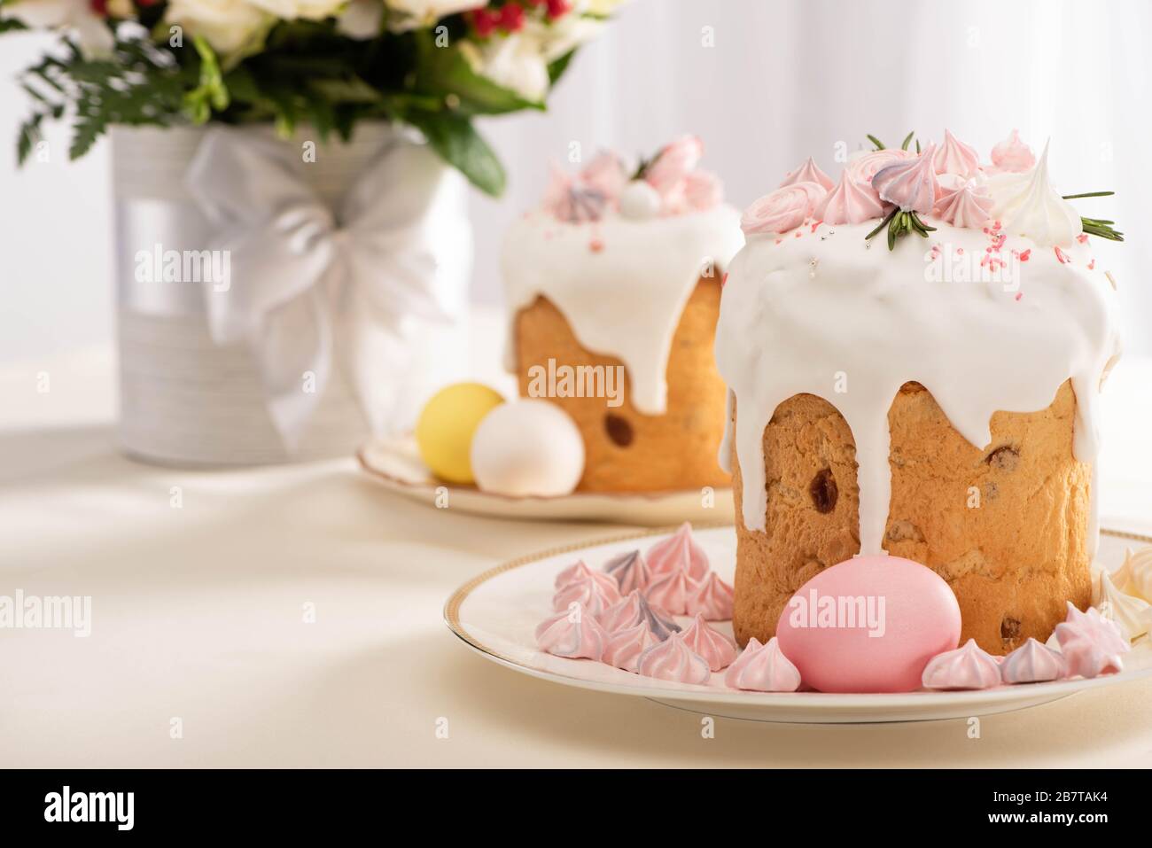 selective focus of festive Easter cake decorated with meringue near painted eggs on plates and flowers Stock Photo