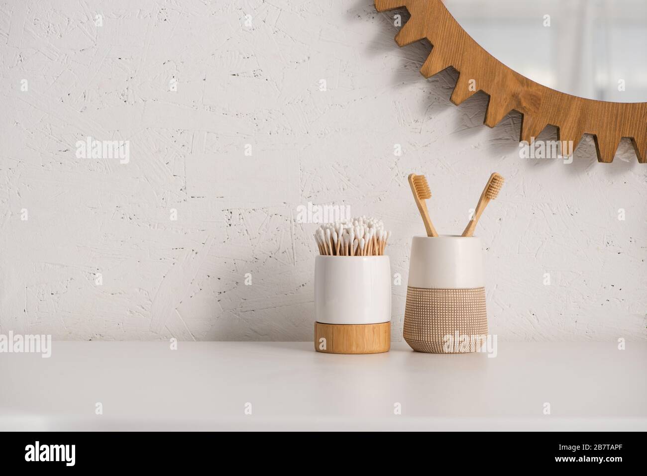 Toothbrush holders with toothbrushes and ear sticks near round mirror