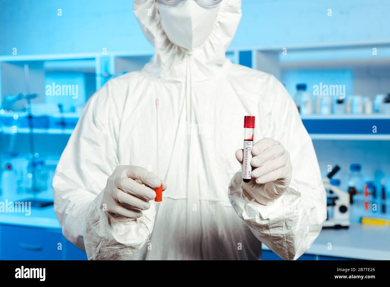 cropped view of scientist in latex gloves and medial mask holding test tube with coronavirus lettering Stock Photo