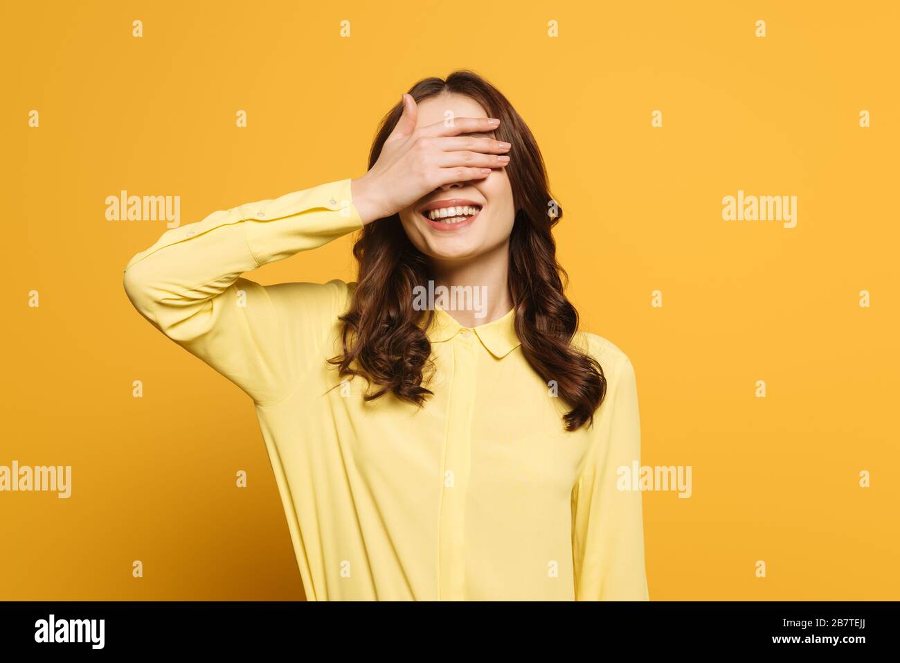 smiling girl covering eyes with hand on yellow background Stock Photo ...