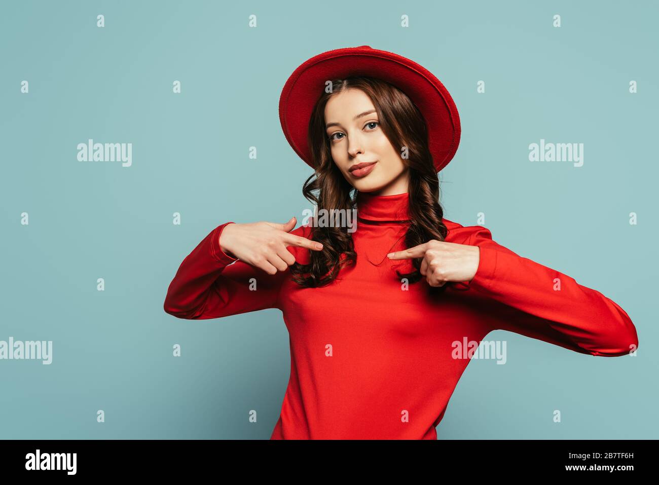 stylish confident girl pointing with fingers at herself while looking at camera on blue
