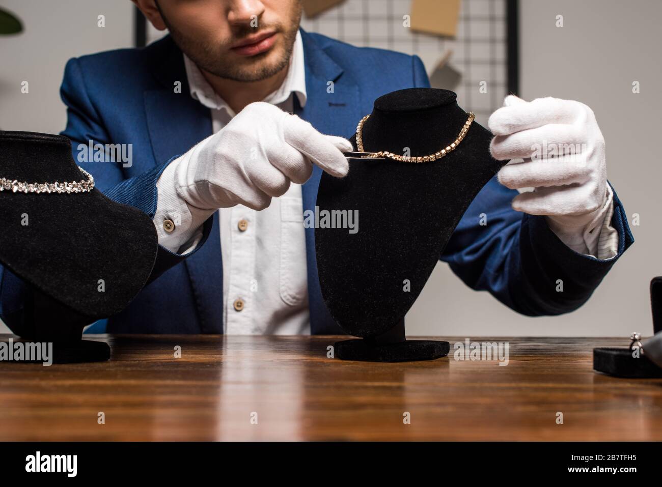 Cropped view of jewelry appraiser in gloves holding tweezers near necklace on necklace stand on table Stock Photo