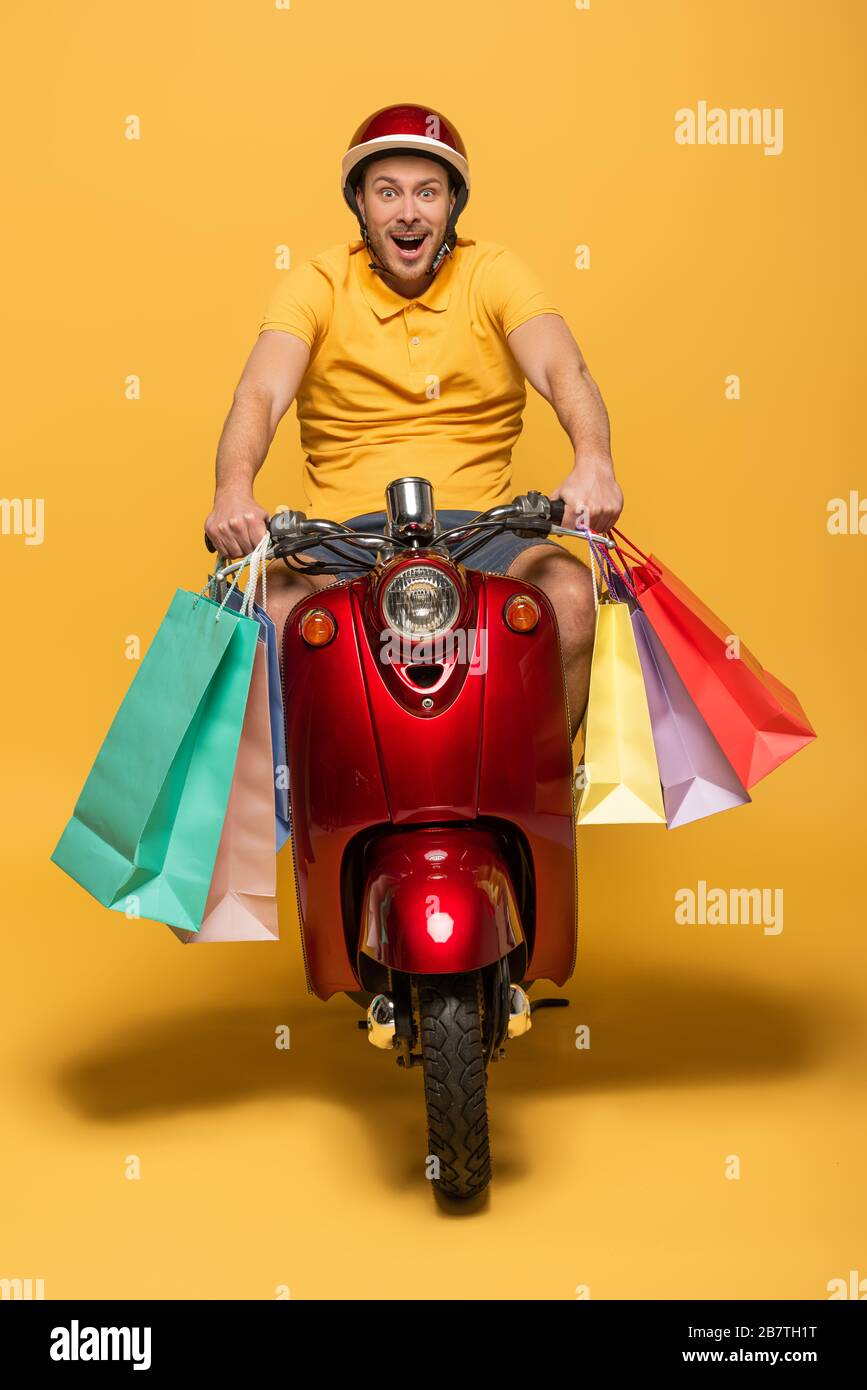happy delivery man in yellow uniform riding scooter with shopping bags ...