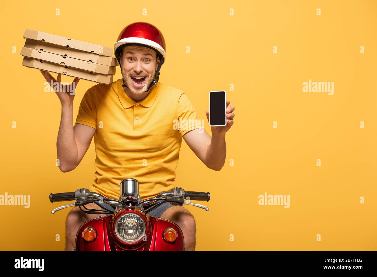 excited delivery man in yellow uniform riding scooter with pizza boxes ...