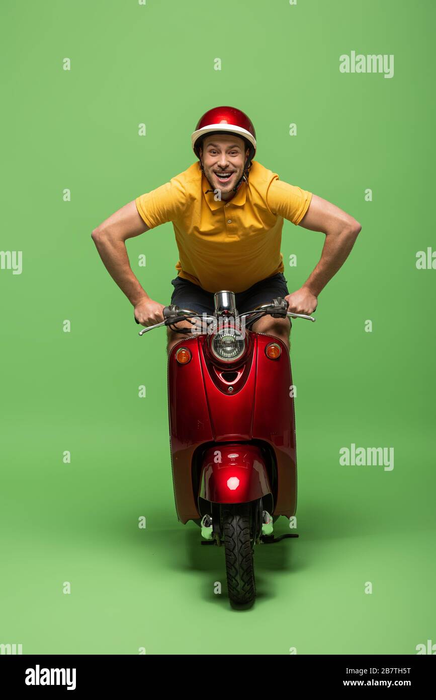 happy delivery man in yellow uniform and helmet on scooter on green ...