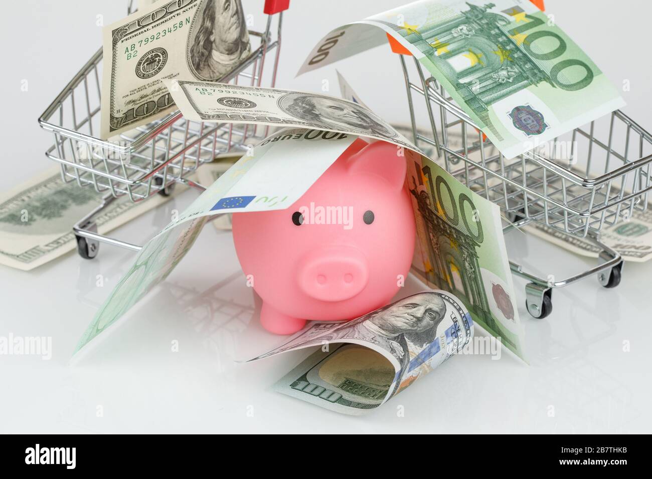 Pink piggy money box in pile of dollar and euro banknotes on gray background Stock Photo