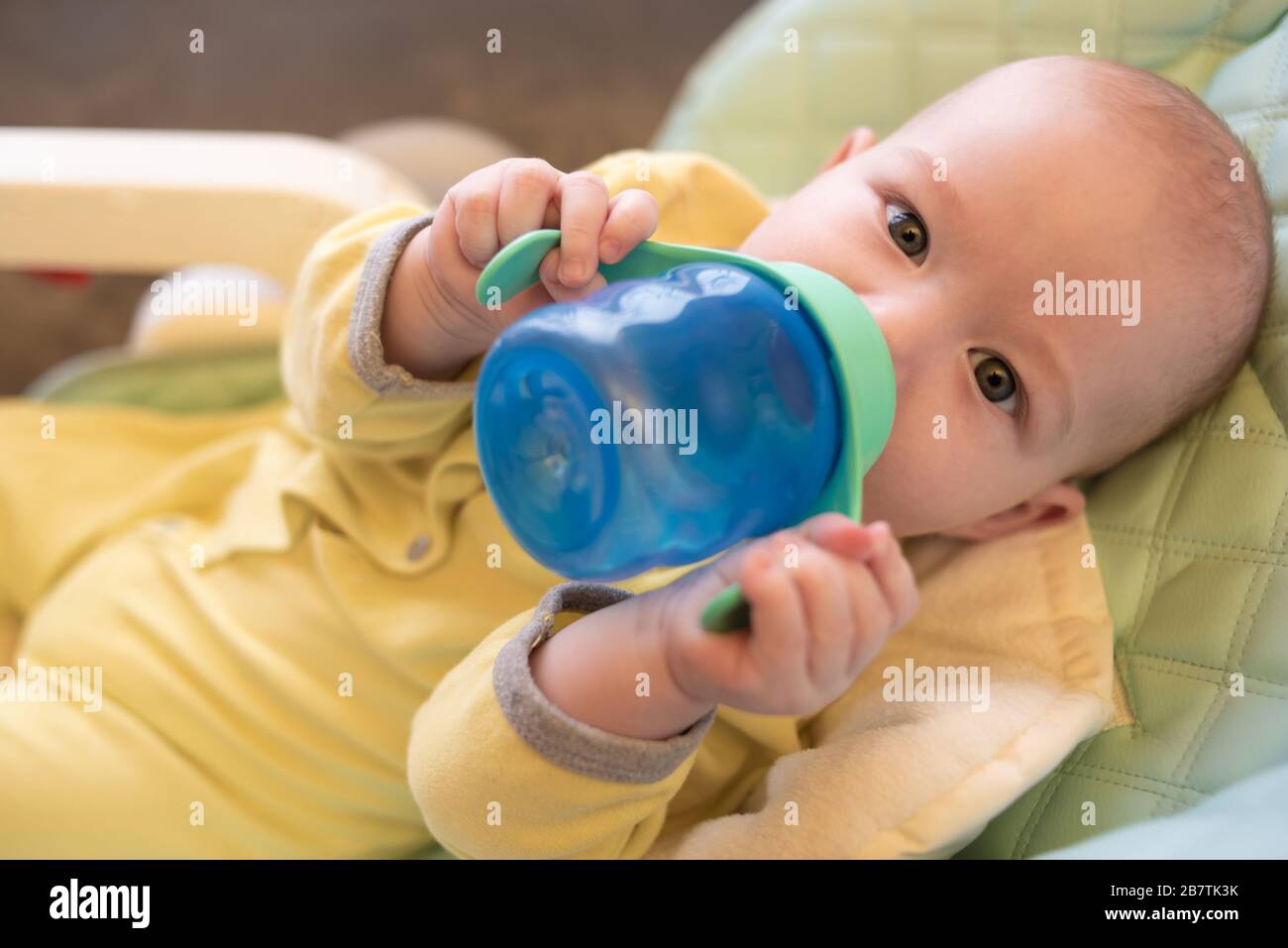 The toddler drinks water from a bottle lying in a high chair for
