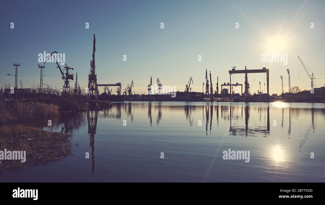 Shipyard cranes silhouettes reflected in water at sunset, color toning applied. Stock Photo