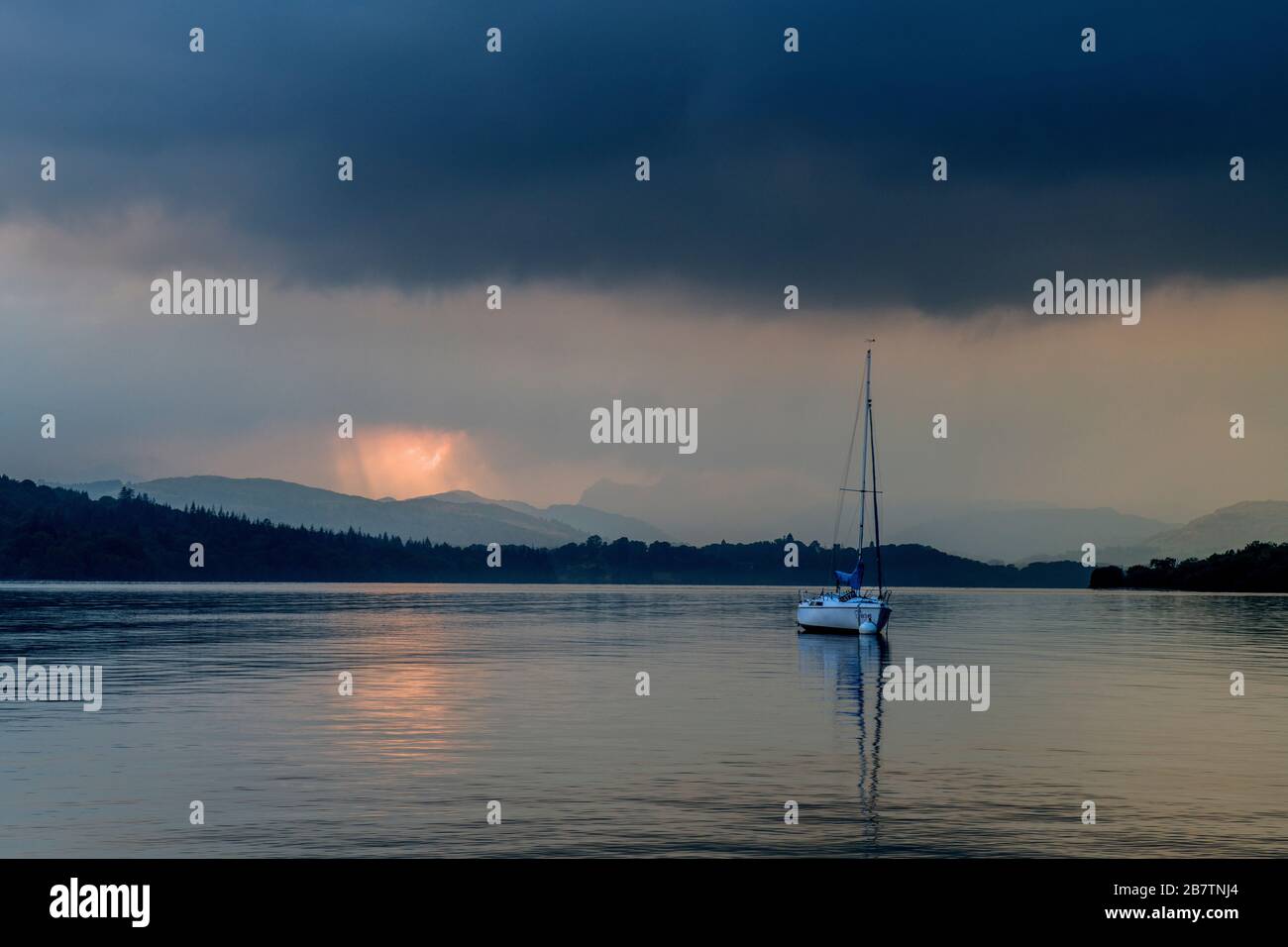 Lake Windermere from Miller Ground beach showing the distant hills, a shaft of sunlight and a moored yacht. That shaft of sunlight lights up the shot. Stock Photo