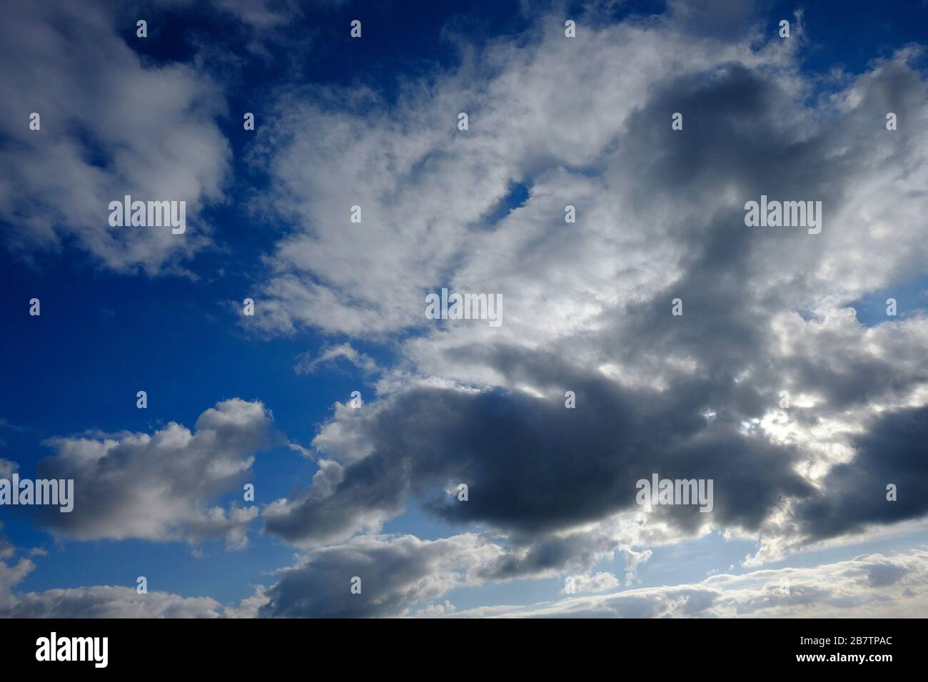 sunlight behind dark clouds on cloudy blue sky background Stock Photo