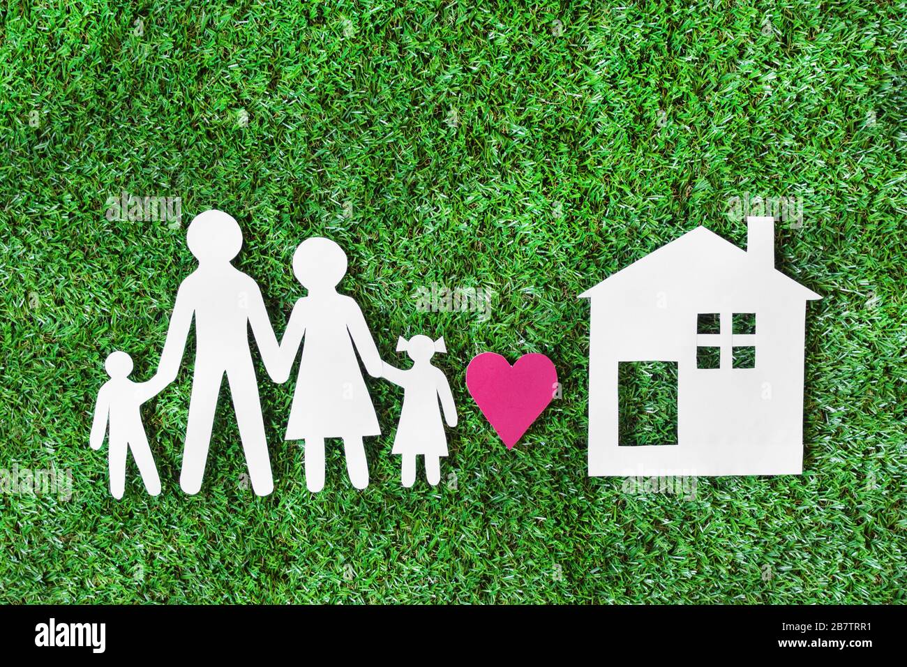 White paper cut of family with house on green grass background top view ...