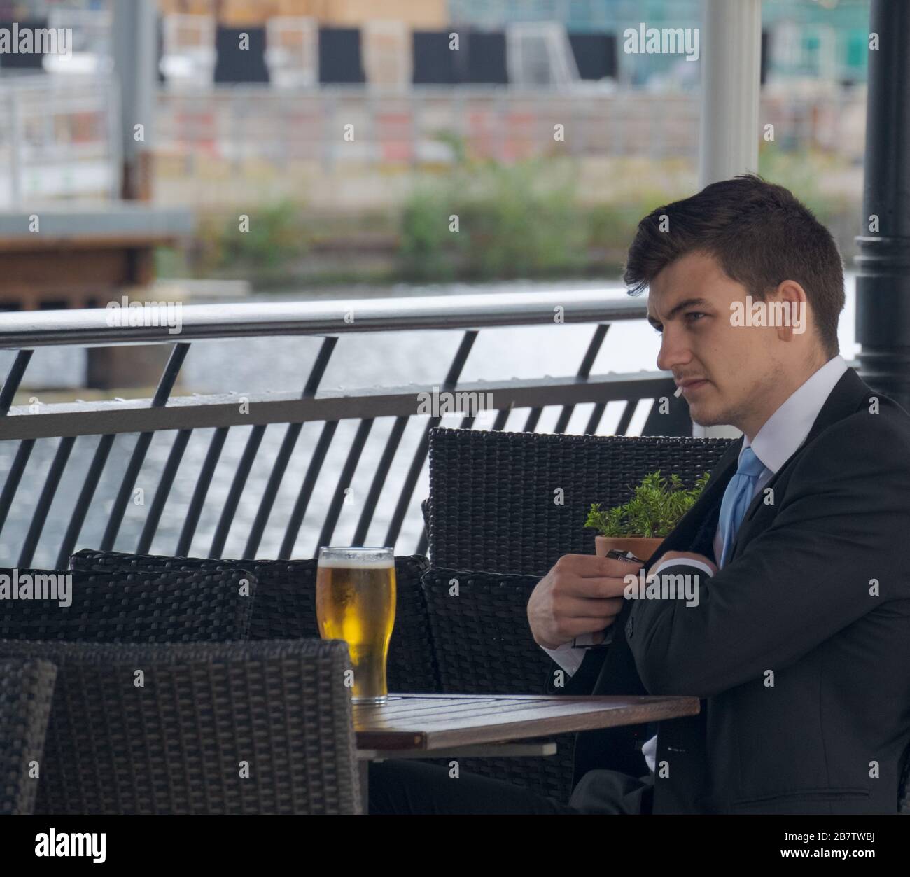 Young business man reaches into his pocket while sitting at outside table with glass of beer at Canary Wharf, London Docklands, UK. Stock Photo
