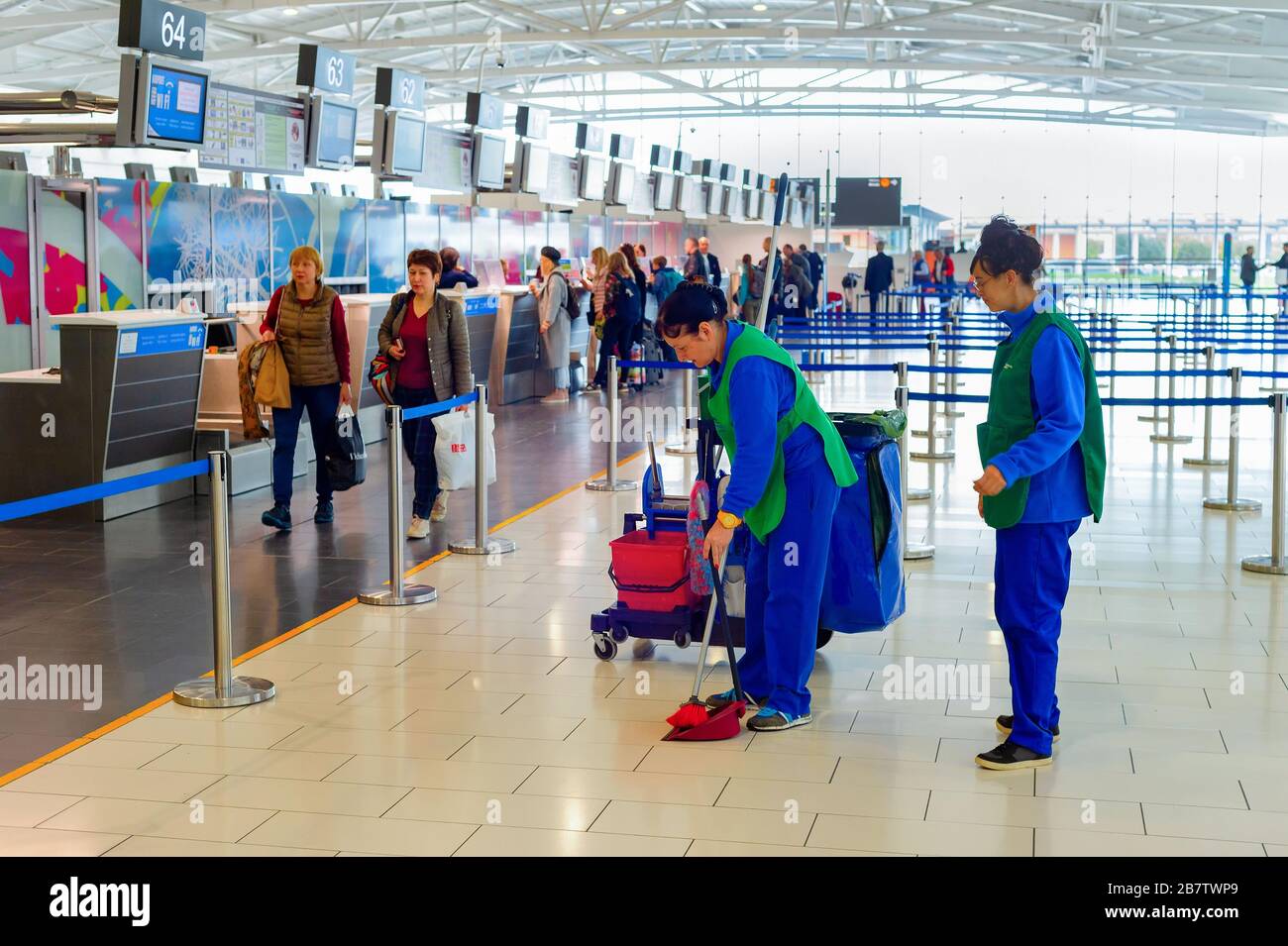 LARNACA, CYPRUS - FEBRUARY 21, 2019: Cleaning women in uniform with broom, scoop and buckets in the international airport terminal, row of people at p Stock Photo