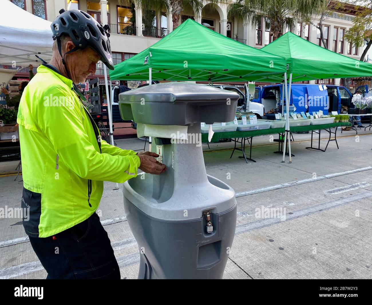 Santa Barbara, California, USA. 17th Mar, 2020. A cyclist in neon jacket who is a long time resident of Santa Barbara tries out the new hand washing station at the FarmerÃs Market: the infection-fighting contraption is a reminder Ã‘ on an otherwise temperate and beautiful Southern California evening Ã‘ that the Corona Virus is coming to town. In spite of the Covid-19 infection scare, Santa Barbara residents and tourists come out to the Tuesday evening FarmerÃs Market on March 17, 2020 to shop for fresh cut flowers, organic vegetables, wheat grass, grass fed meats, honey, olive oils, etc. Stock Photo