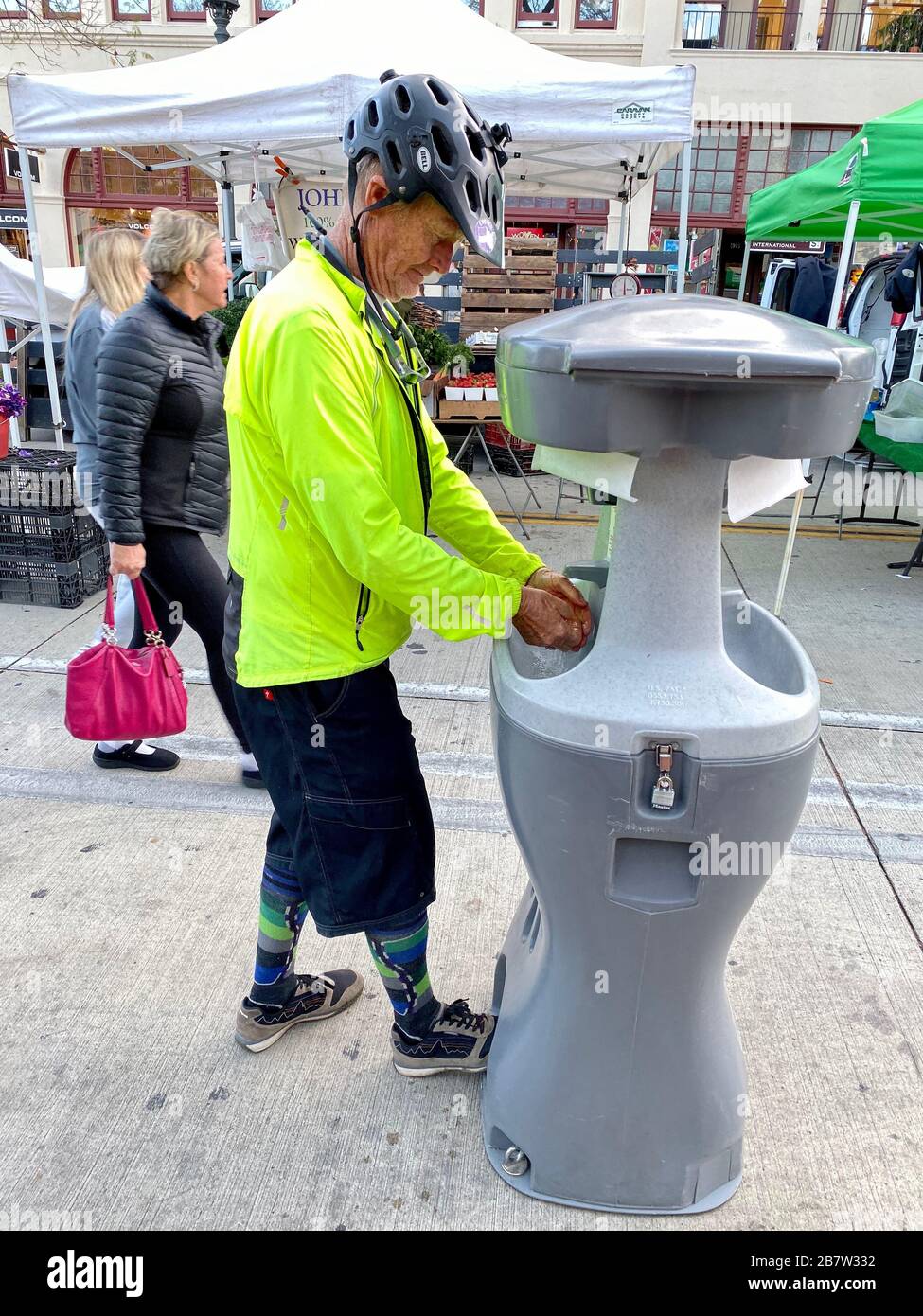 Santa Barbara, California, USA. 17th Mar, 2020. A cyclist in neon jacket who is a long time resident of Santa Barbara tries out the new hand washing station at the FarmerÃs Market: the infection-fighting contraption is a reminder Ã‘ on an otherwise temperate and beautiful Southern California evening Ã‘ that the Corona Virus is coming to town. In spite of the Covid-19 infection scare, Santa Barbara residents and tourists come out to the Tuesday evening FarmerÃs Market on March 17, 2020 to shop for fresh cut flowers, organic vegetables, wheat grass, grass fed meats, honey, olive oils, etc. Stock Photo