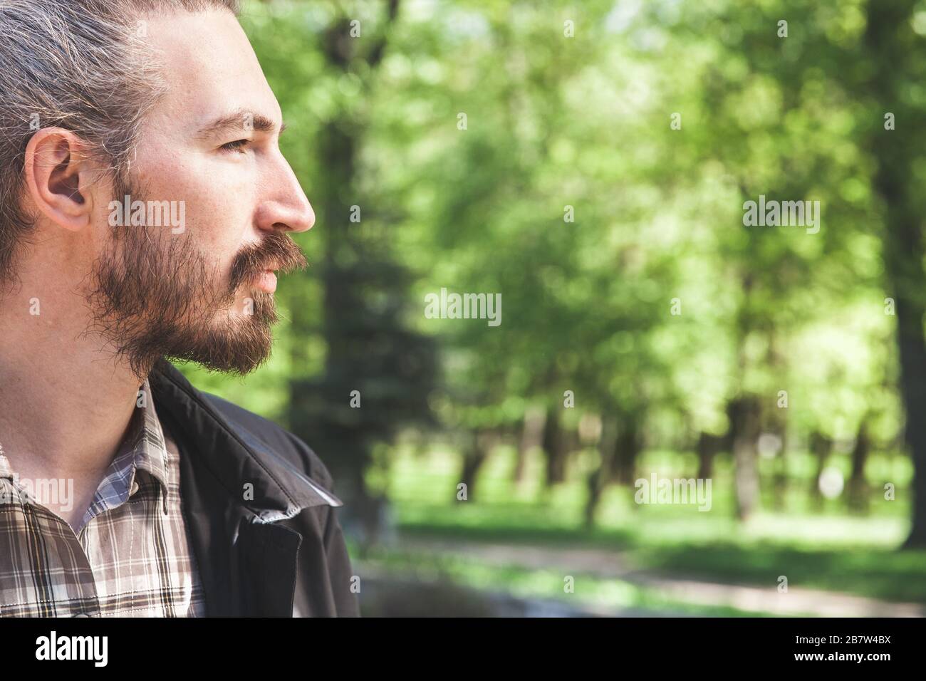 Young adult bearded Asian man, close up outdoor profile portrait photo taken at sunny summer day in a park Stock Photo