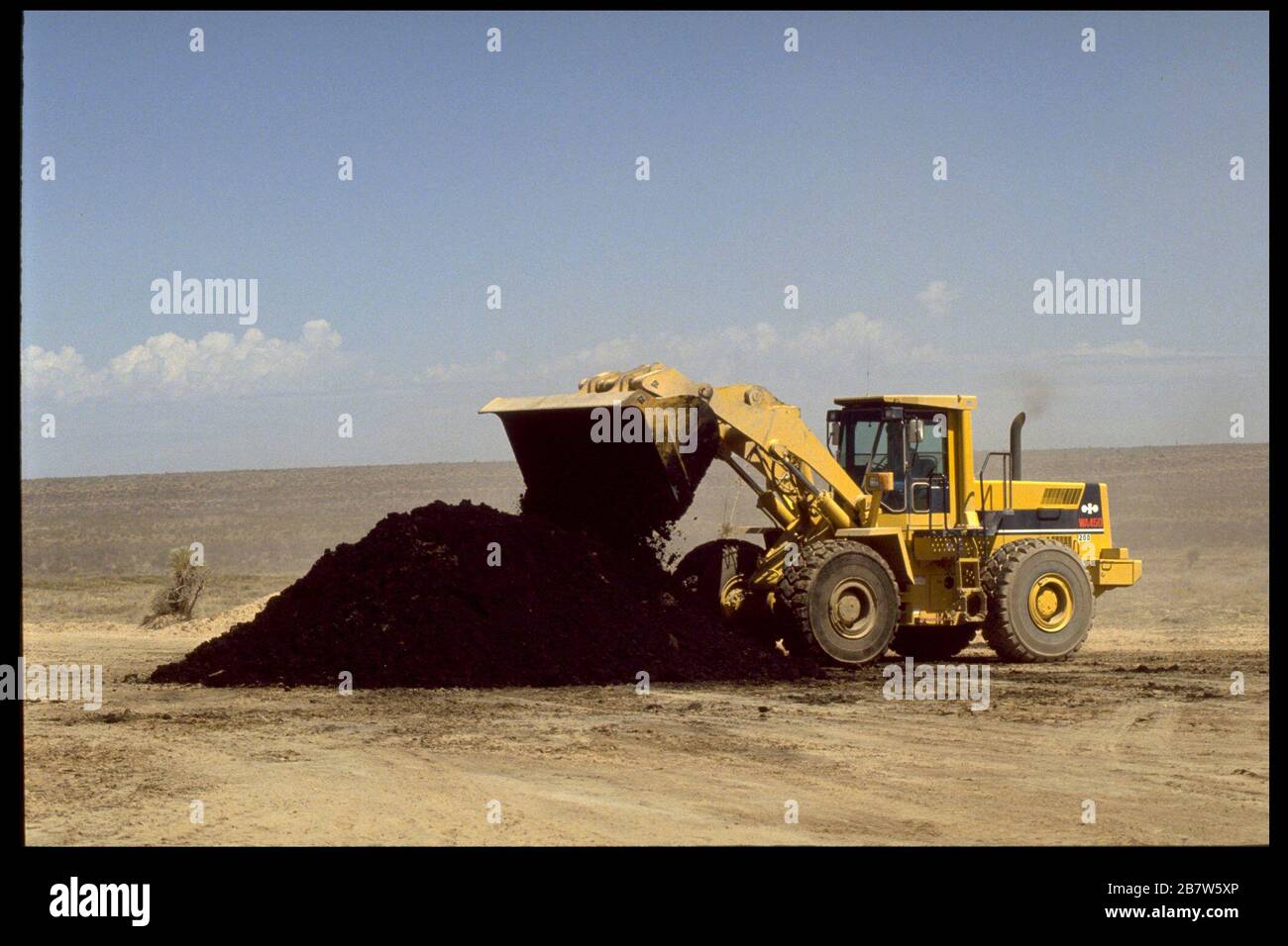 Sierra Blanca Texas USA, 1995: Front-loader excavator spreads sewer sludge from New York City on MERCO-owned ranchland near Sierra Blanca. ©Bob Daemmrich Stock Photo