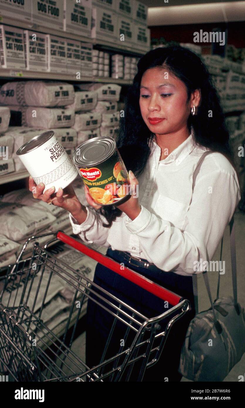 Austin Texas USA: Asian-American woman comparing generic and brand-name canned peaches at grocery store. MR ©Bob Daemmrich Stock Photo