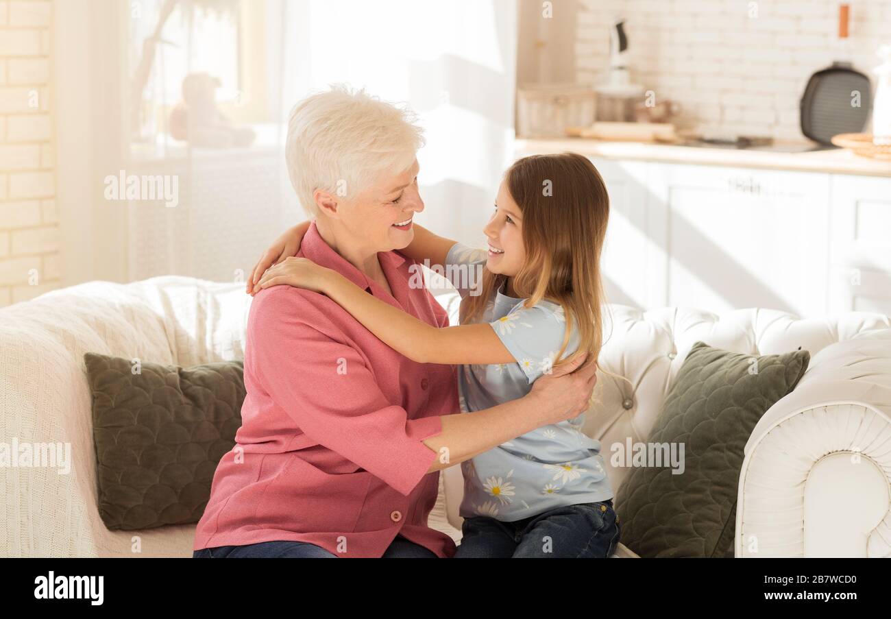 Little child and her grandmother hugging each other on sofa Stock Photo