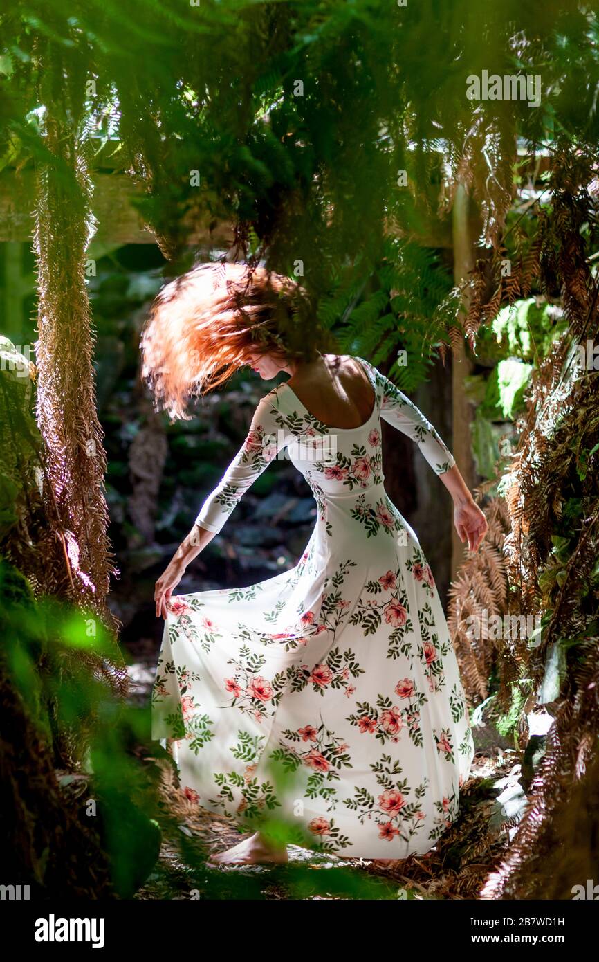 Woman in Floral Dress Tossing Hair amongst Fern Trees in Forest Stock Photo