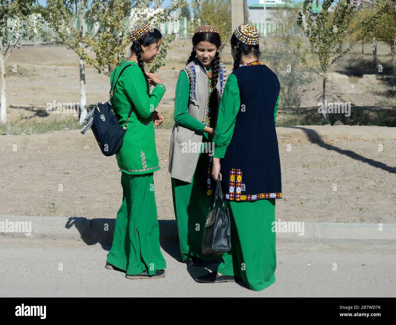 Three student young girls with braids wearing Turkmenistan national dress used as school uniform in Kunya Urgench. Long green dress and tekke hat. Stock Photo
