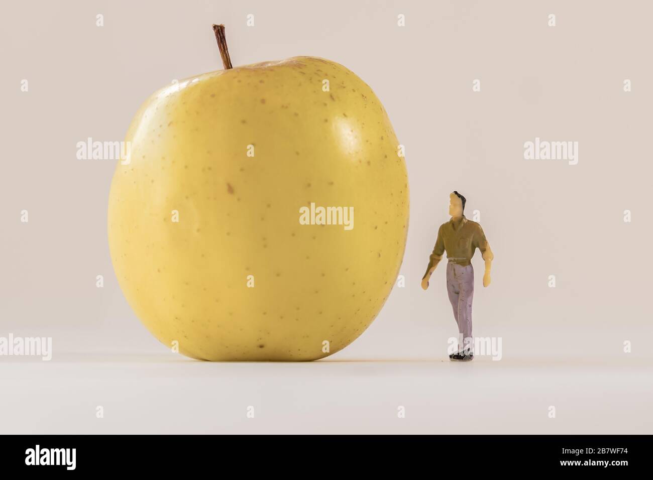 Miniature man figure standing next to big yellow apple. Shallow depth of field background. Healthcare, healthy lifestyles and slimming concept. Stock Photo