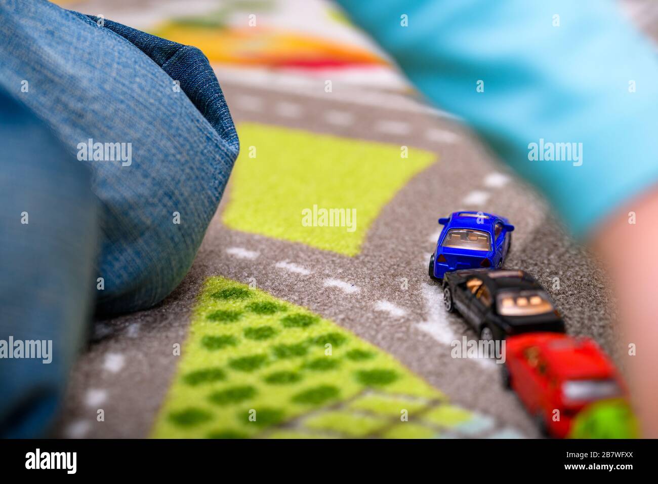 Close-up of five year old boy playing and lining up toy cars on a playing mat with roads. The cars have vivid colors. Stock Photo
