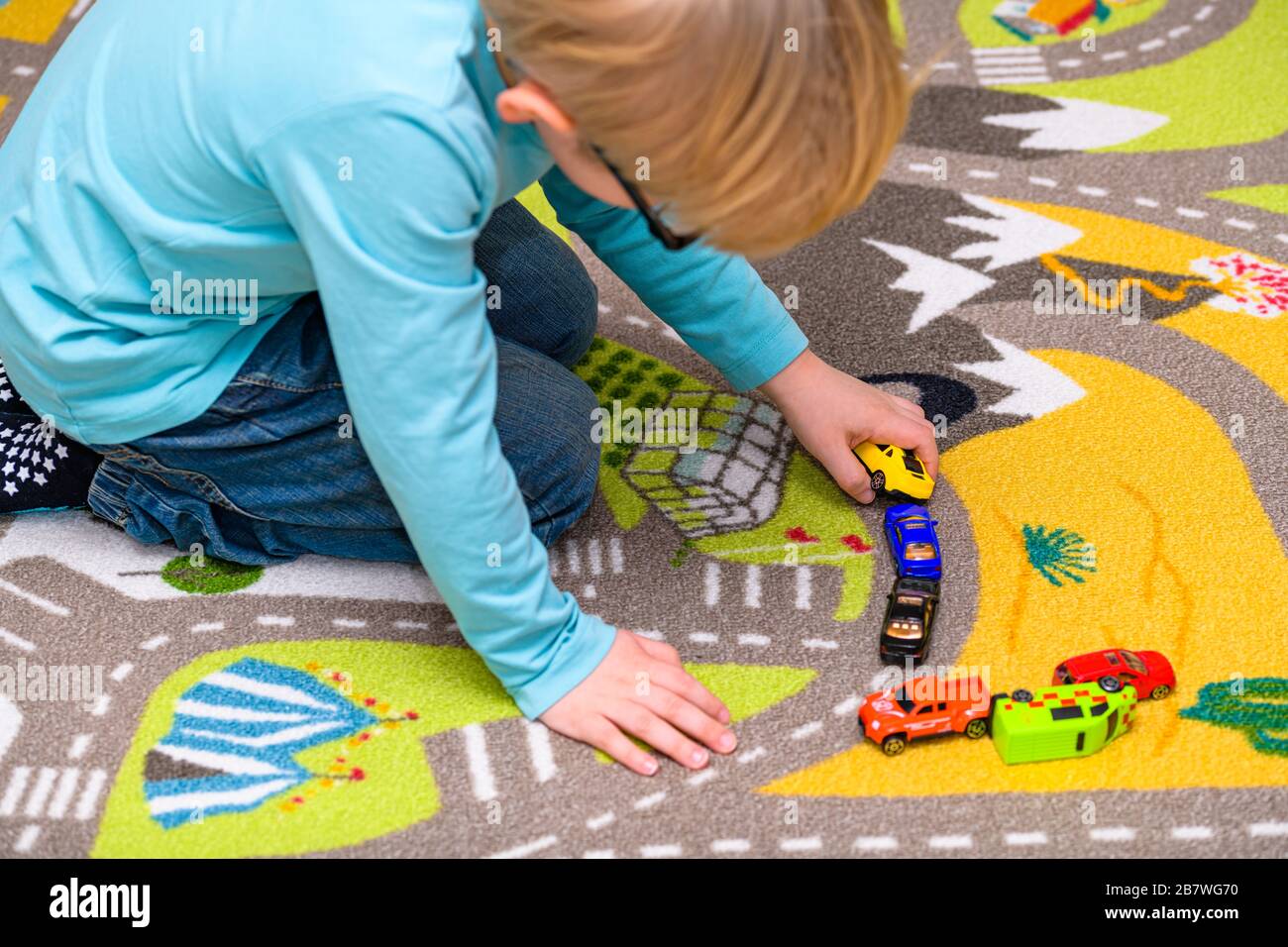 Five year old boy playing and lining up toy cars on a playing mat with
