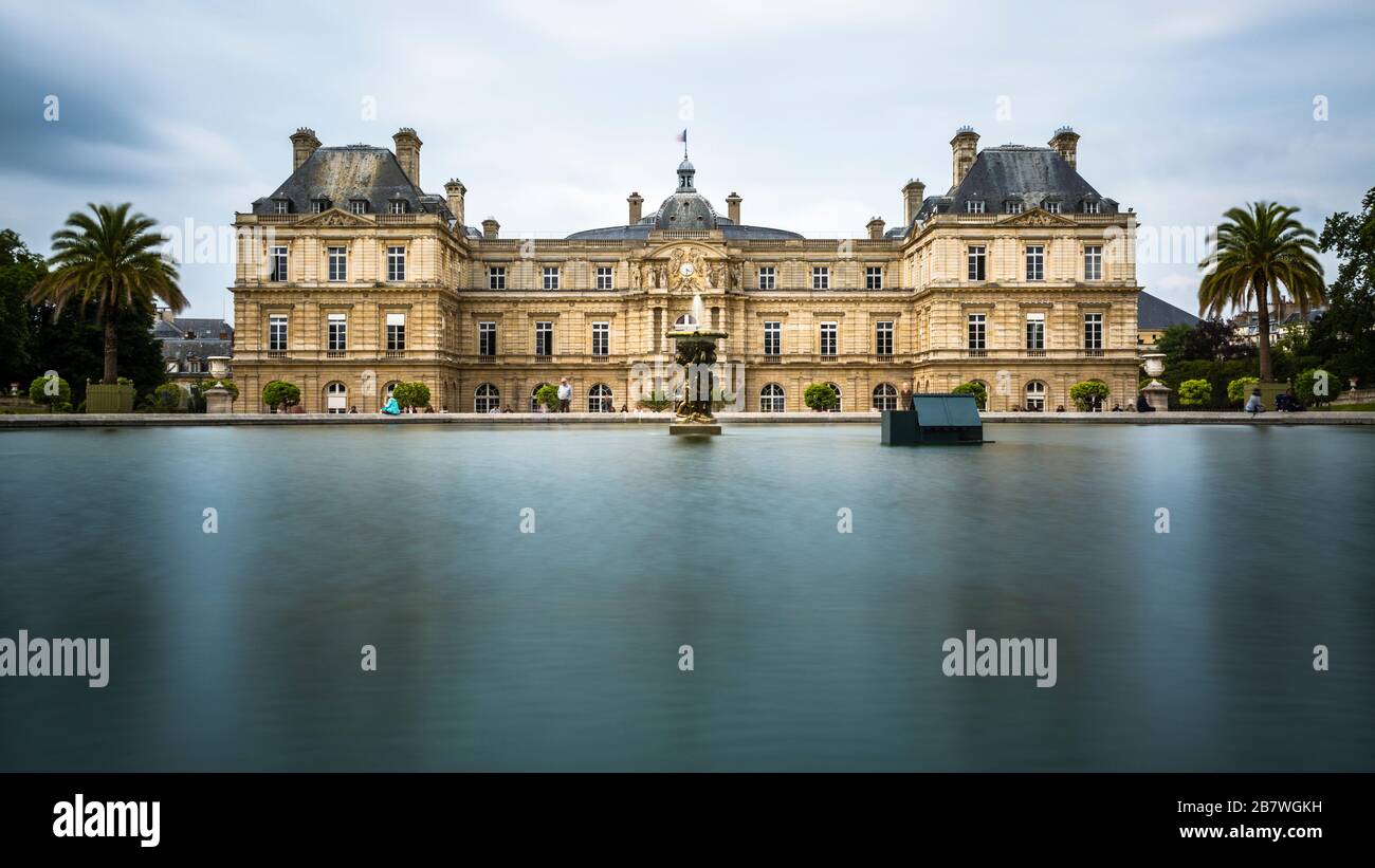 A long exposure of the Luxembourg Palace in Luxembourg Gardens in Paris, France in a cloudy day with the garden's lake in the foreground. Stock Photo