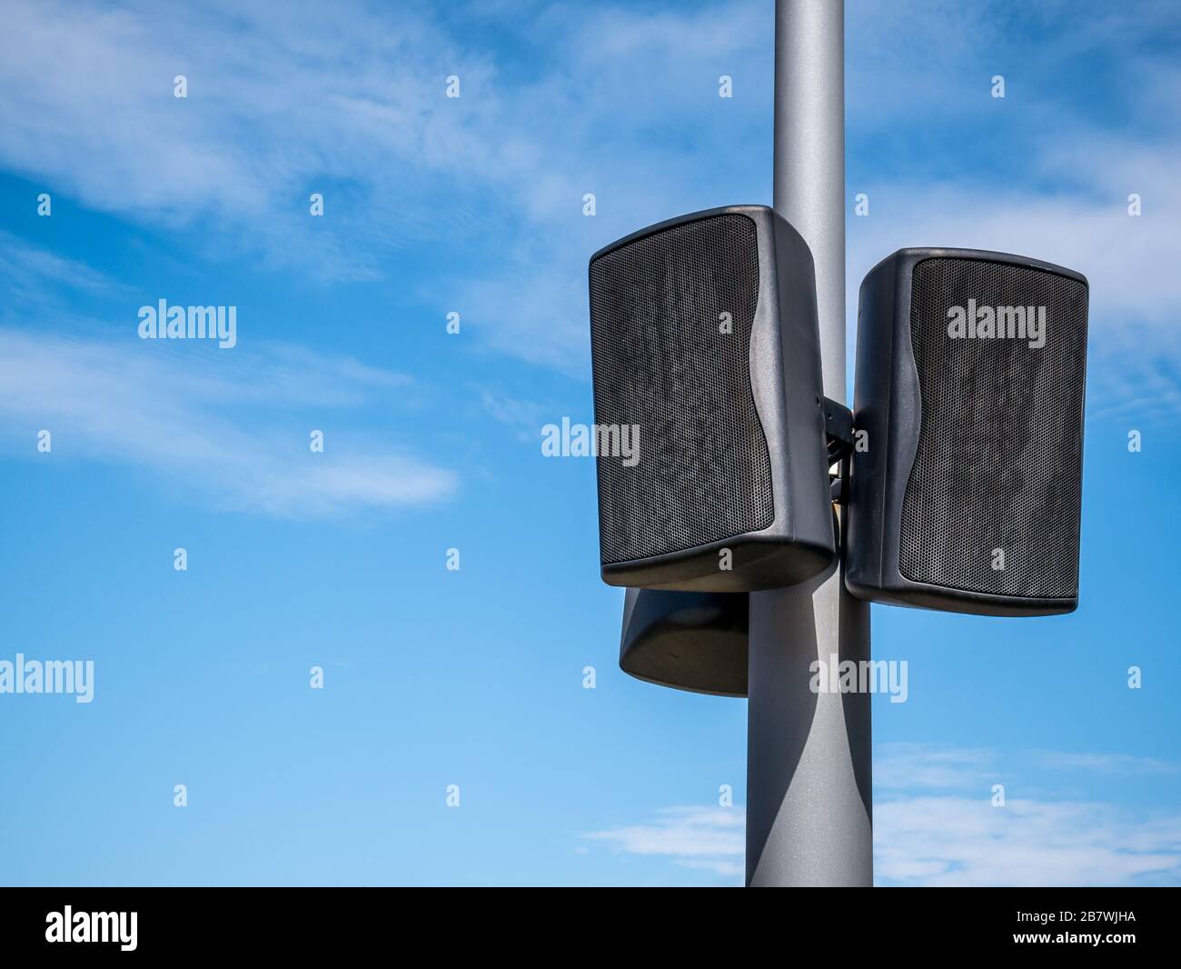 Black speakers suspended from a metal pole with blue sky as a background. Outdoor  speakers for music Stock Photo - Alamy