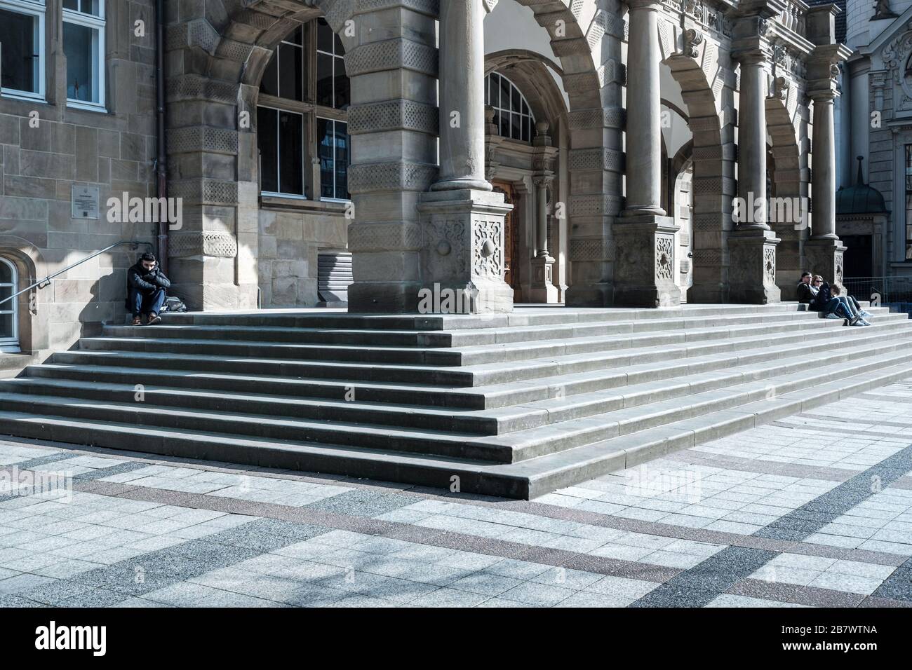 people sitting on stairs of city hall in Bielefeld, Germany. there's a lot of space between the people, symbolizing current coronavirus crisis Stock Photo