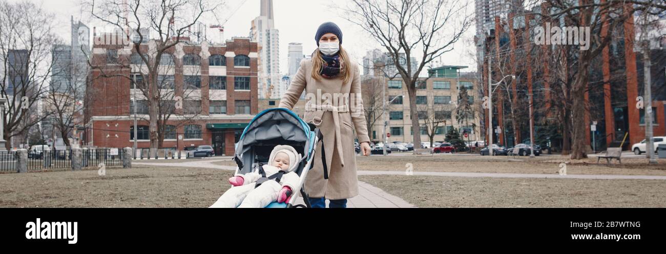 Caucasian mother in surgical mask walking with baby outdoor in Toronto. Protective face mask against Chinese pneumonia COVID-19 epidemic virus disease Stock Photo