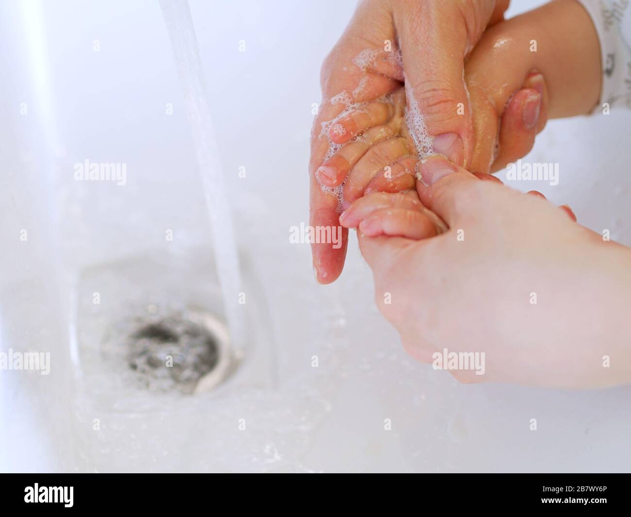 Close up, baby and adult washing hands with a soap in a sink with a tap water during the Coronavirus outbreak, for prevention. Stock Photo