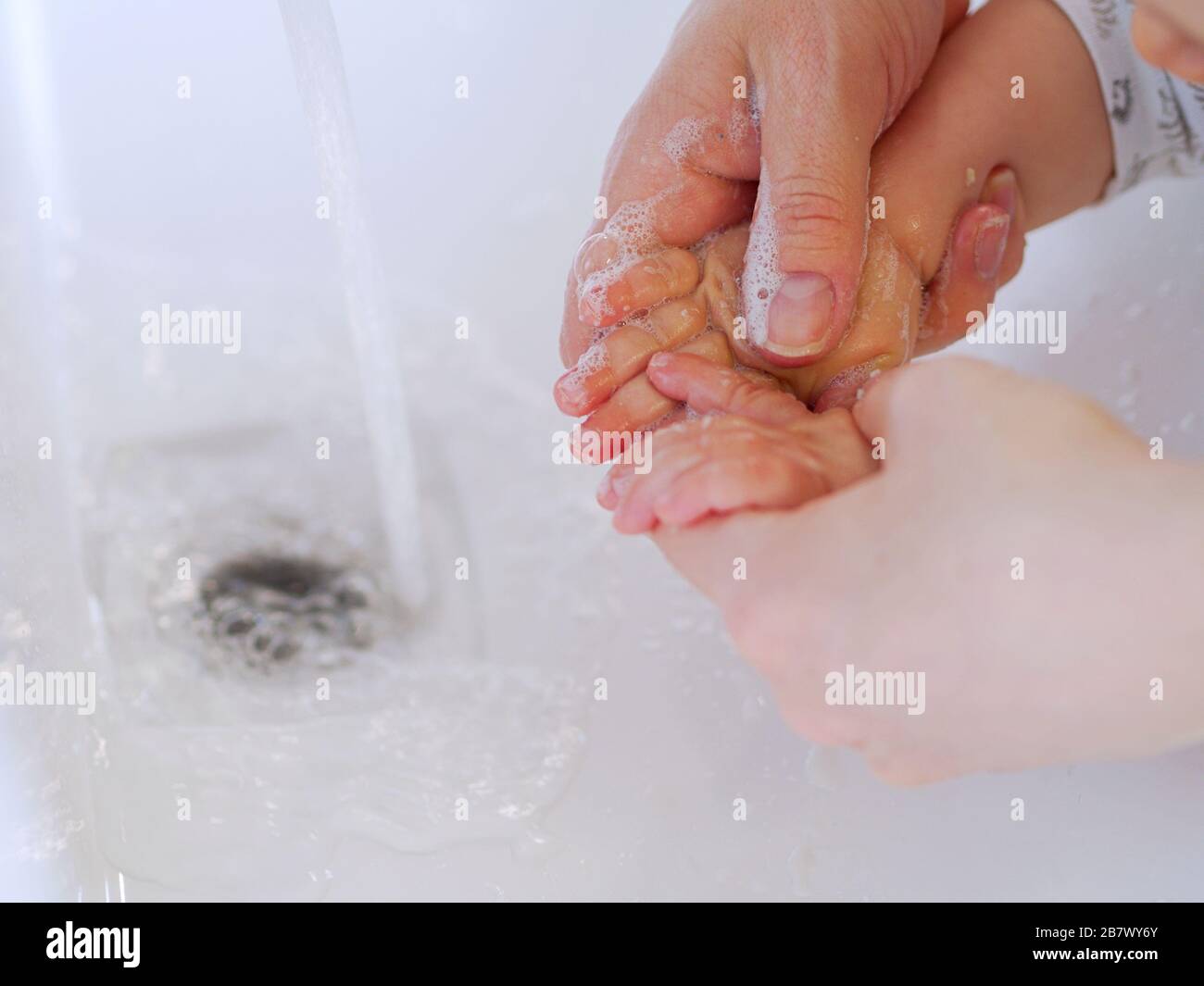 Close up, baby and adult washing hands with a soap in a sink with a tap water during the Coronavirus outbreak, for prevention. Stock Photo