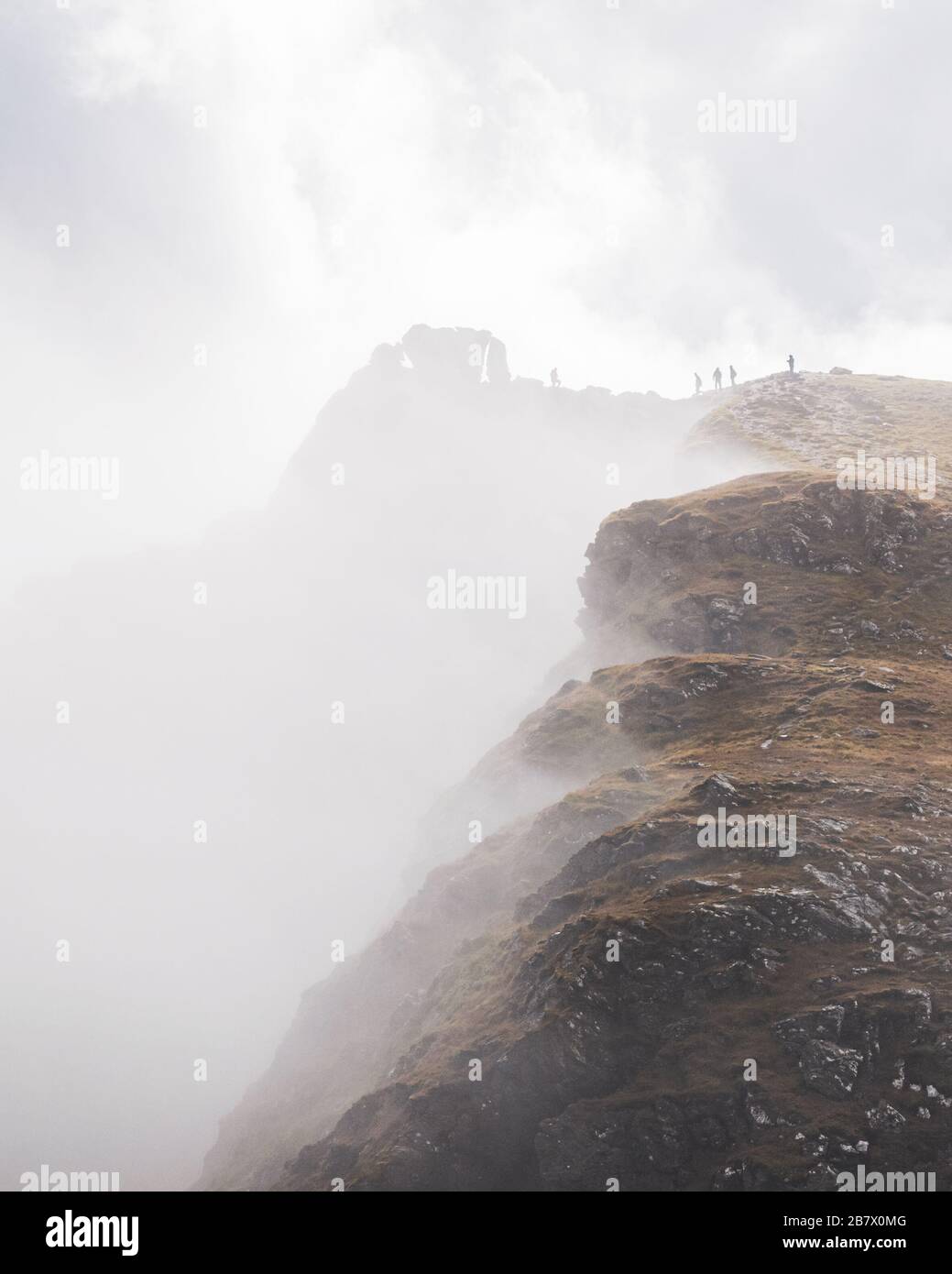 Silhouettes of five hillwalkers on the top of the Cobbler with rugged cliffs in deep fog. Dramatic Scottish landscape. Stock Photo
