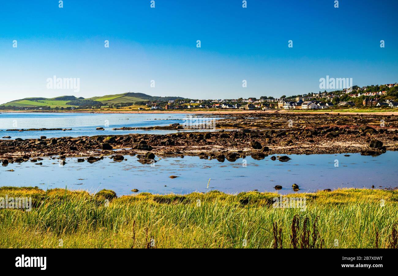 Picturesque tranquil village of Seamill, Scotland seen across the rocky beach at low tide. Scenic Scottish coastal landscape. Stock Photo