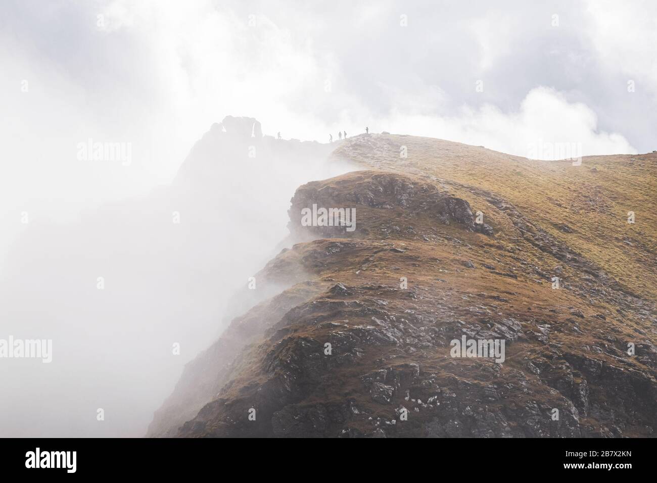 Silhouettes of five hillwalkers on the top of the Cobbler with rugged cliffs in deep fog. Dramatic Scottish landscape. Stock Photo