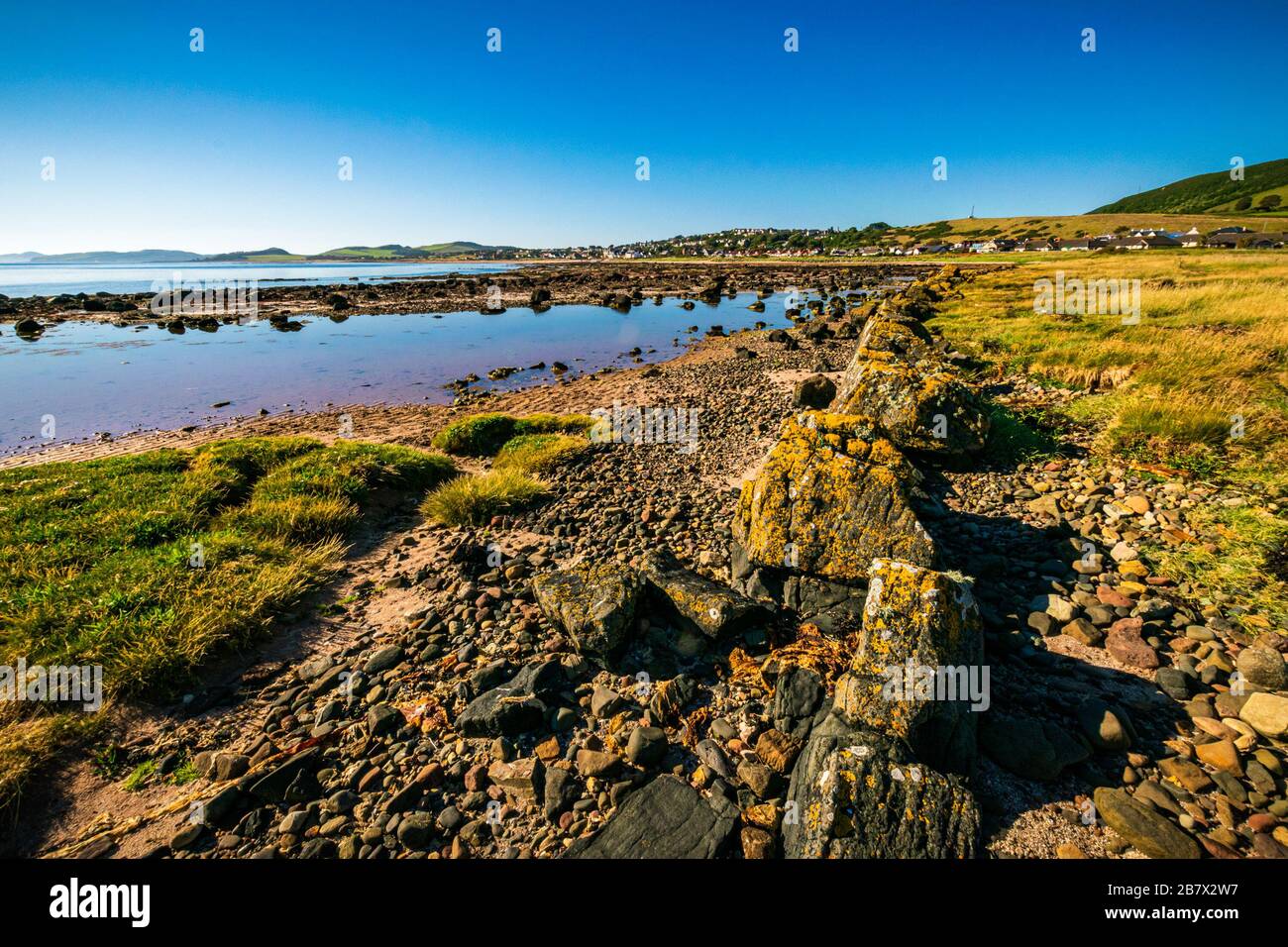 Afternoon sun at the picturesque rocky beach near the Scottish village of Seamill in Firth of Clyde on a clear summer afternoon. Stock Photo