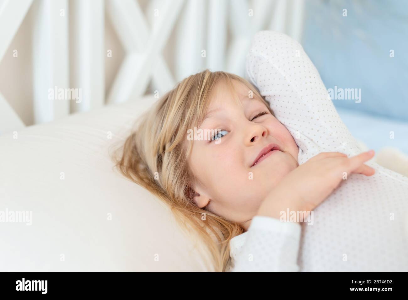 Cute adorable caucasian blond little toddler kid girl lying in bed on white  pillow. Adorable sweet happy smiling child wink at wake up early morning  Stock Photo - Alamy