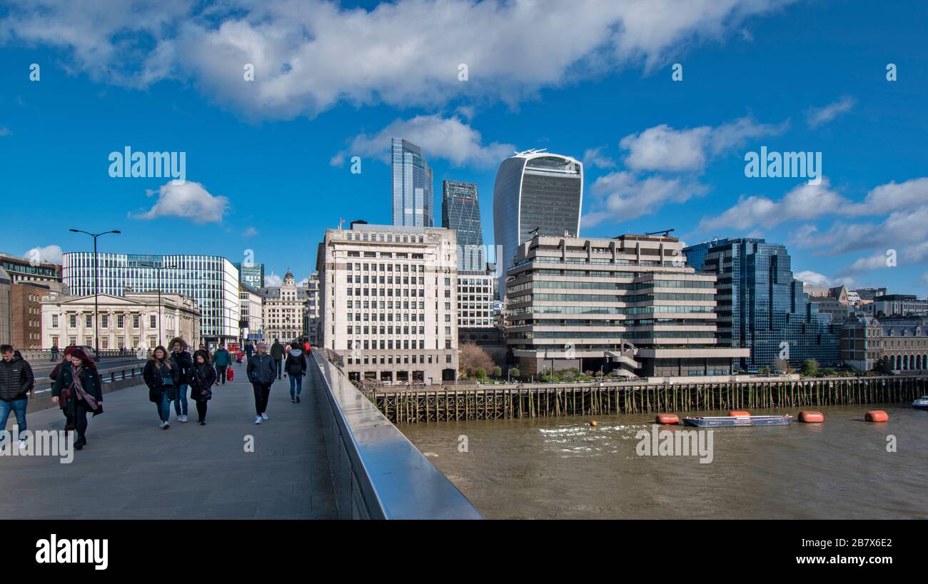 LONDON BRIDGE AND TOURISTS VIEW ACROSS TO BUILDINGS ON LOWER THAMES STREET AND THE GROUP OF WALKIE TALKIE AND CHEESGRATER SKYSCRAPERS Stock Photo