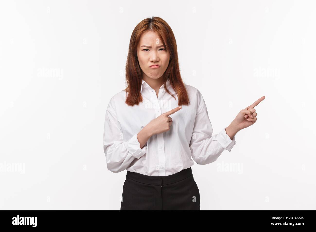 Portrait of displeased and unsatisfied asian young woman in shirt, grimacing and frowning with disgust and disappointment, pointing right at something Stock Photo