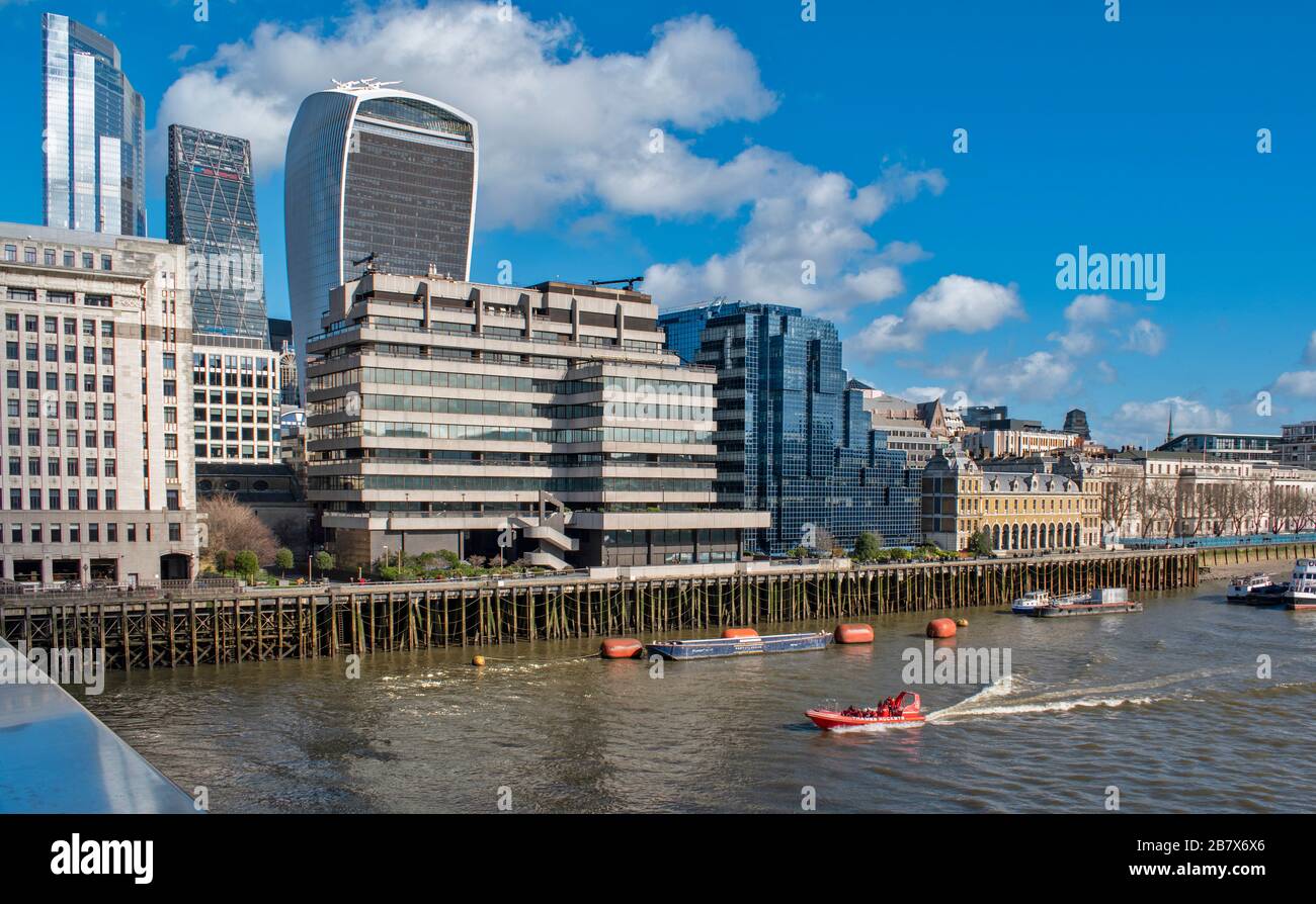 LONDON RED BOAT ON THE RIVER THAMES A VIEW ACROSS TO BUILDINGS ON LOWER THAMES STREET AND THE GROUP OF WALKIE TALKIE AND CHEESGRATER SKYSCRAPERS Stock Photo