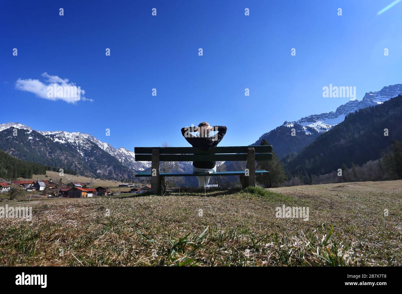 Bad Hindelang, Germany. 18th Mar, 2020. A female hiker enjoys the sunshine and the view of the panorama of the mountains on a bench in the Hintersteiner Valley. Credit: Karl-Josef Hildenbrand/dpa/Alamy Live News Stock Photo