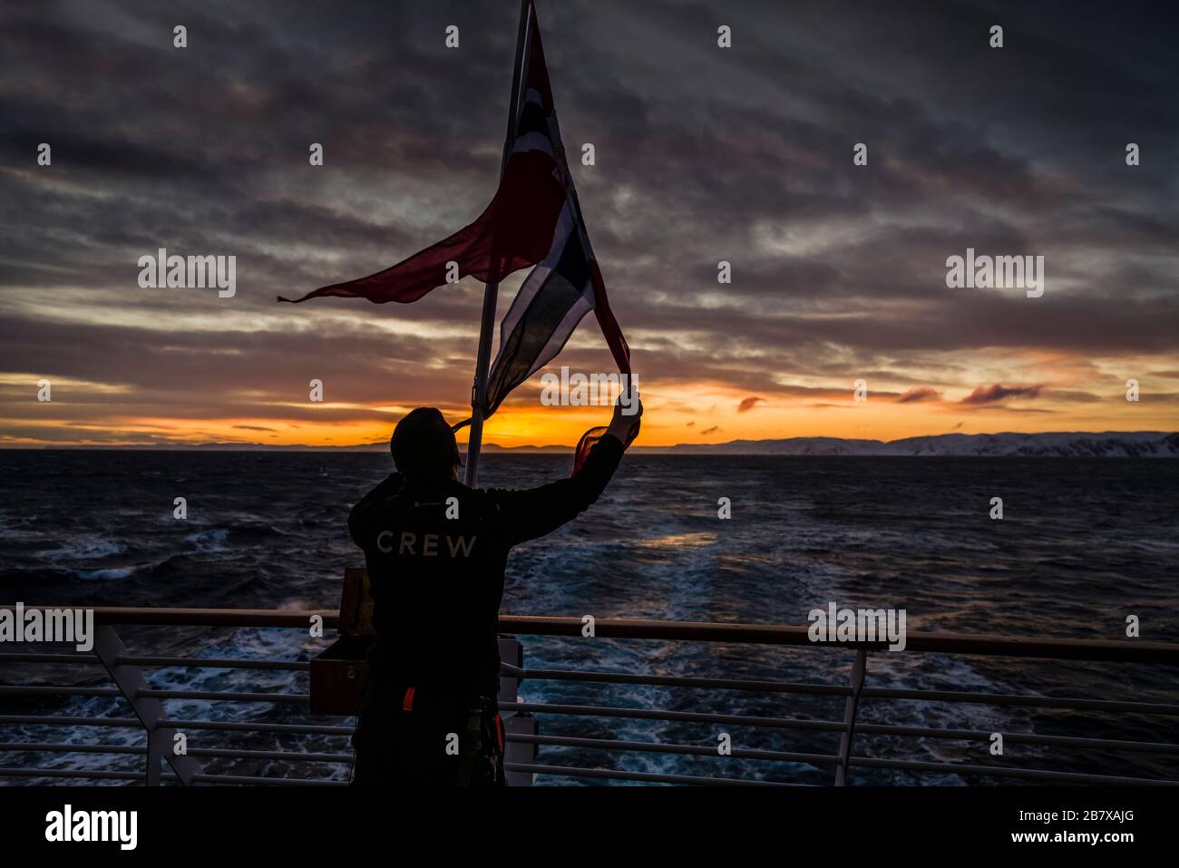 Hurtigruten crew bring in the flag at sunset, Honningsvag, Norway. Stock Photo