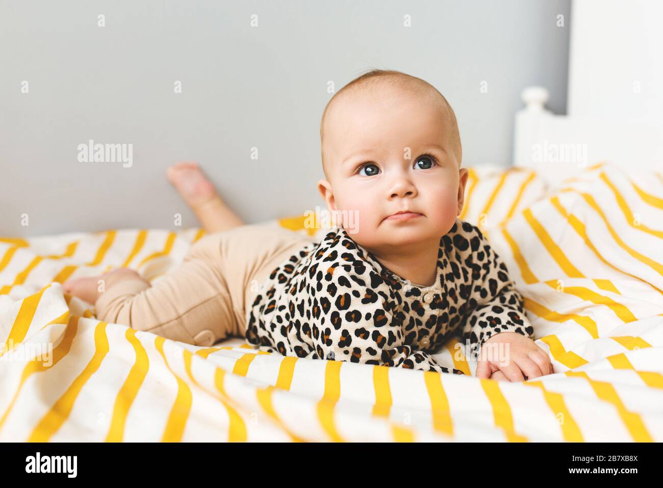 Happy baby with cute smile sitting in a cot. Child sitting in the bed. Happy childhood. Stock Photo